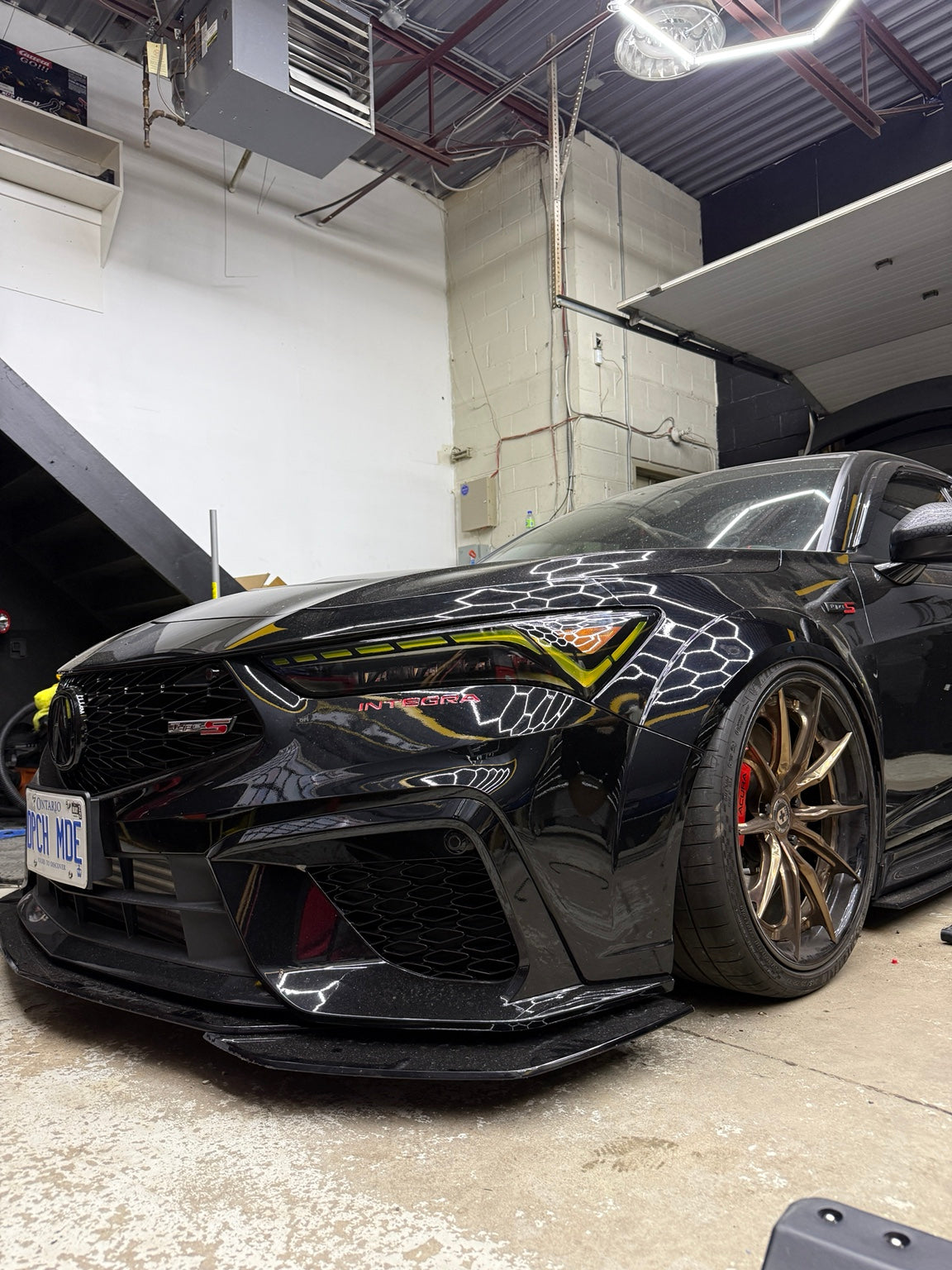 Black Acura Integra Type S aired out on ONAIR air suspension, with bronze wheels and red brake calipers inside the workshop.