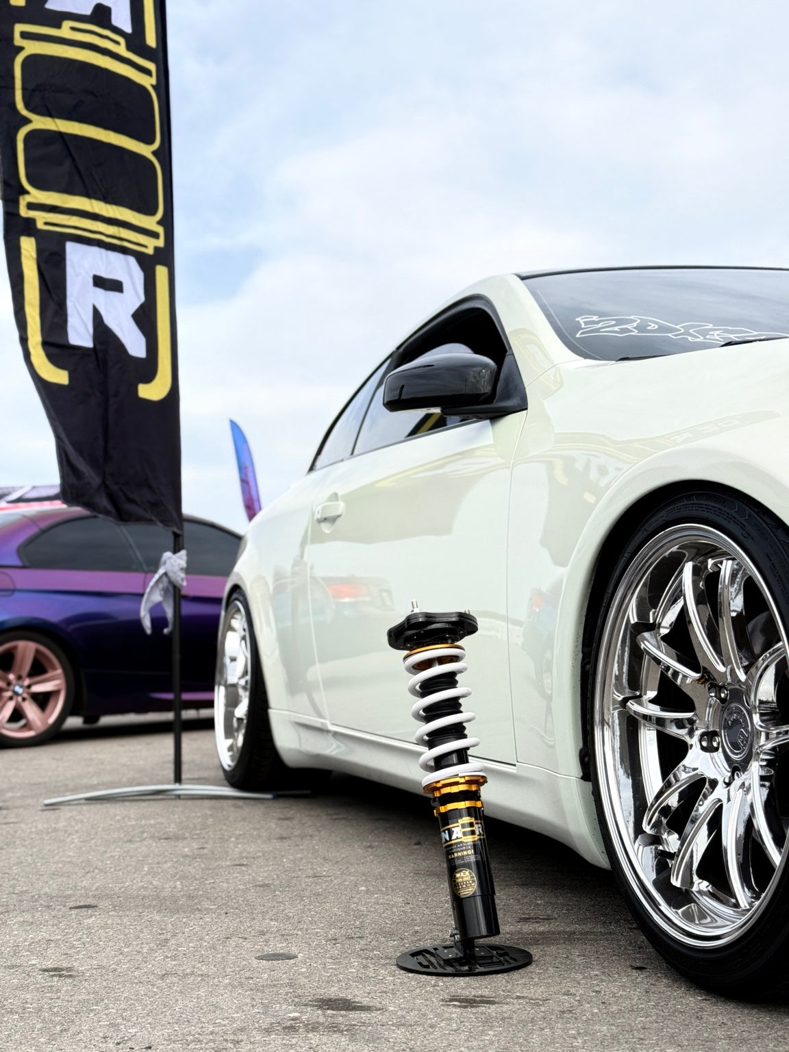 ONAIR gold coilover with a white spring displayed beside a white coupe at an ONAIR event