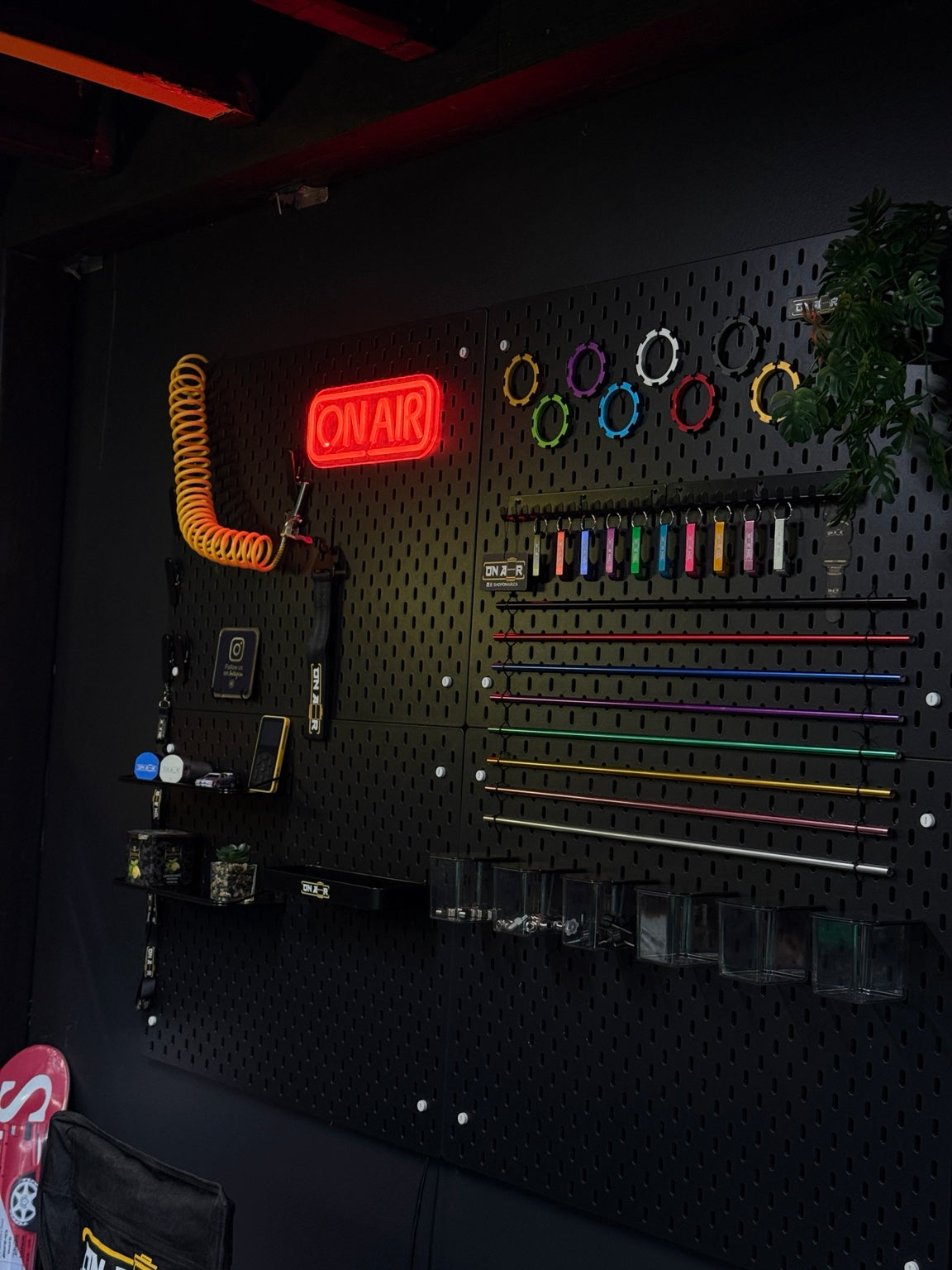 Image of ONAIR shop display wall with a red neon sign, colourful adjustment collars, keychains, hardlines and fittings.