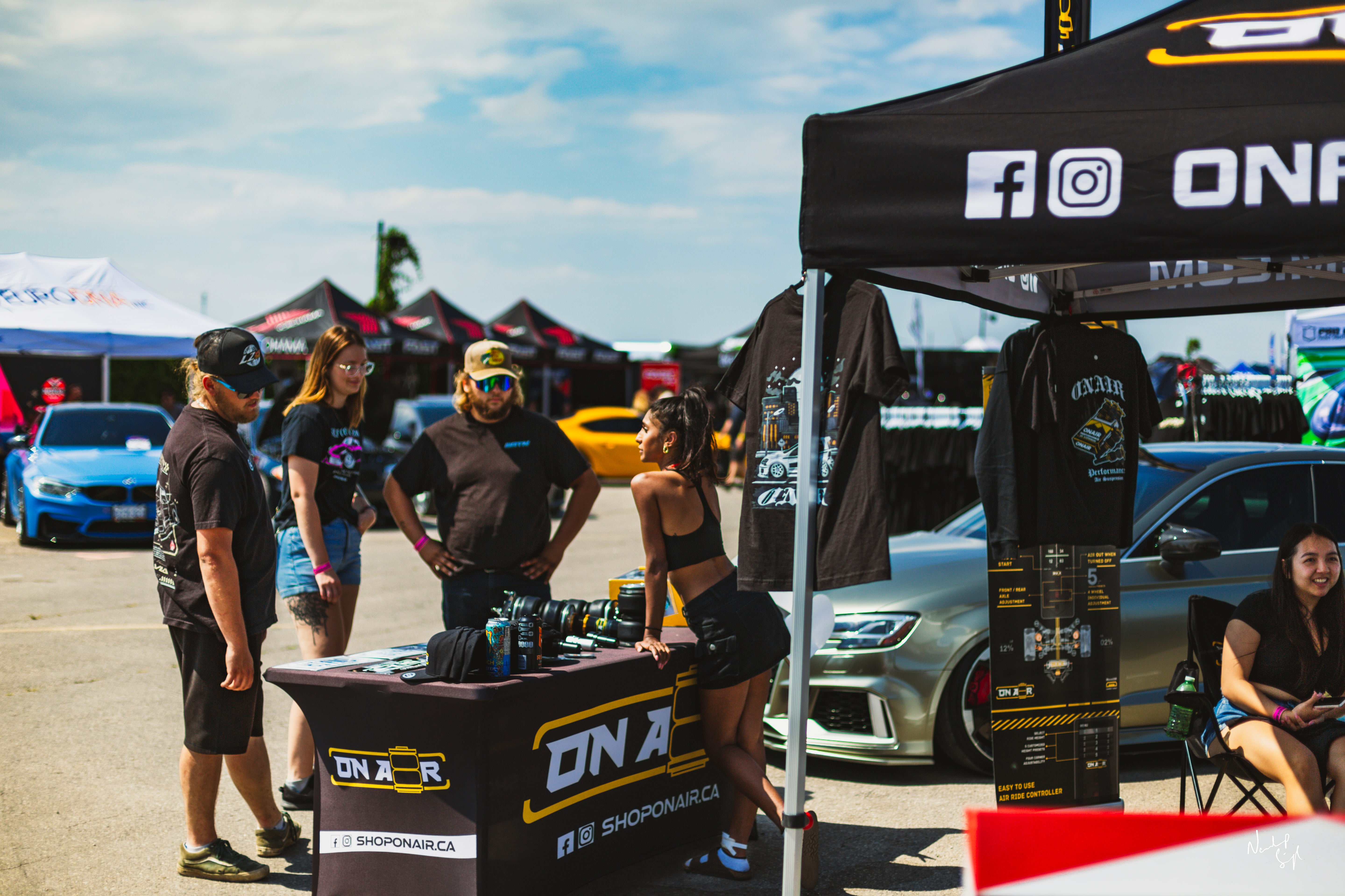 Image of Safia from onair answering questions to guests that were curious about onair. shot features lots of onair merch, bagged air audi, tshirts, air suspension, bags, and other friendly people